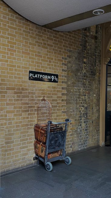 A trolley loaded with several brown cardboard boxes and a patterned fabric bag, positioned against a yellow brick wall near a sign reading 'Platform 9 3/4' at Kings Cross station. The trolley has a black metal frame with two small wheels at the front and two larger wheels at the back, and is situated on a concrete floor under a ceiling with a circular light fixture. This scene depicts a moving or luggage transfer process associated with home relocation or furniture transport, with the trolley ready for loading or unloading. The environment appears to be an interior station area, reflecting the logistical steps involved in professional removals services offered by Man and Van King's Cross.